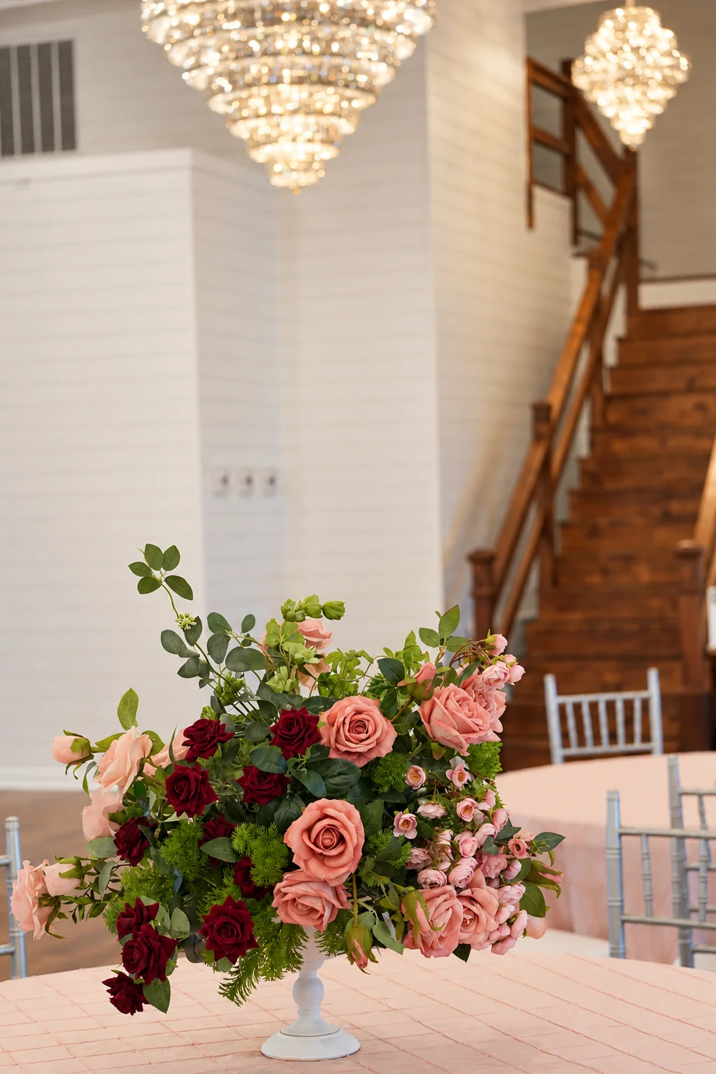 Pink and burgundy flower arrangement beneath chandeliers in the ballroom