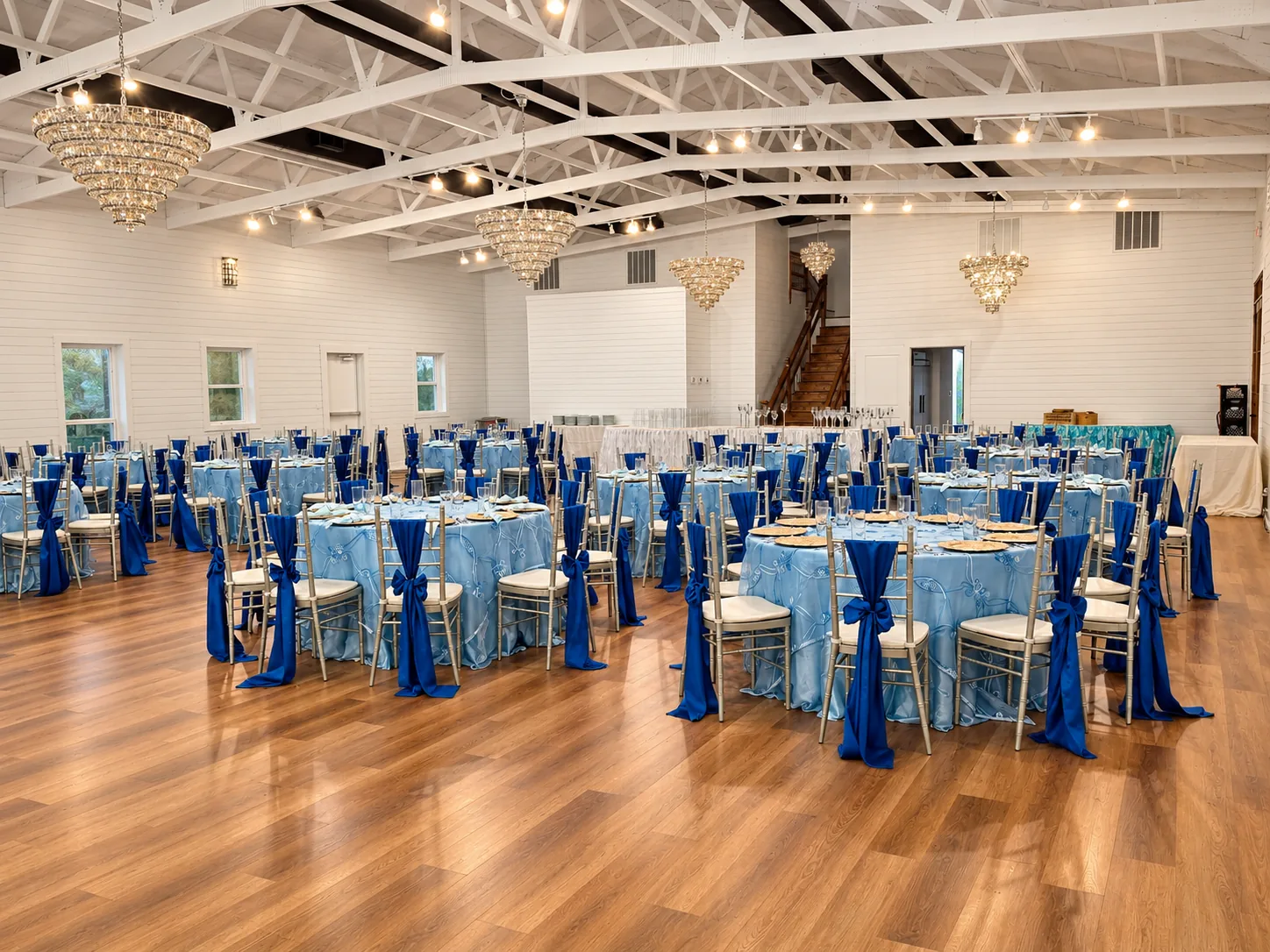 Wide view of the ranch ballroom with white beams, chandeliers, wood flooring, and banquet tables
